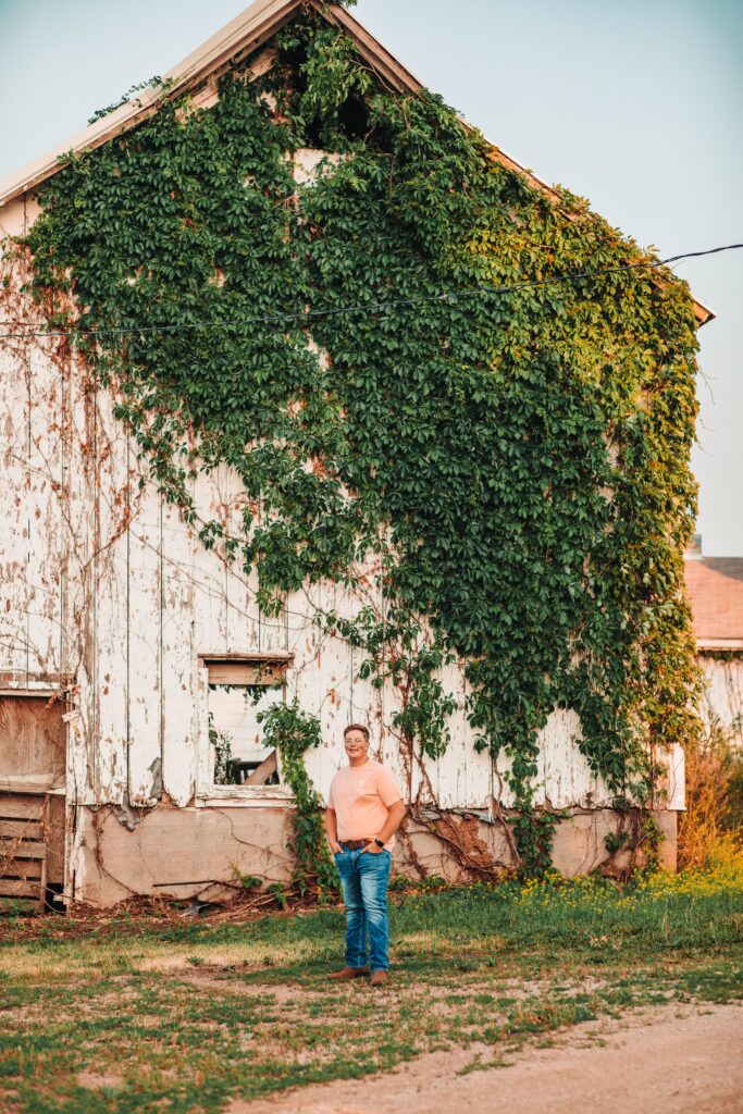 A high school senior standing next to an old barn during his senior photography experience.