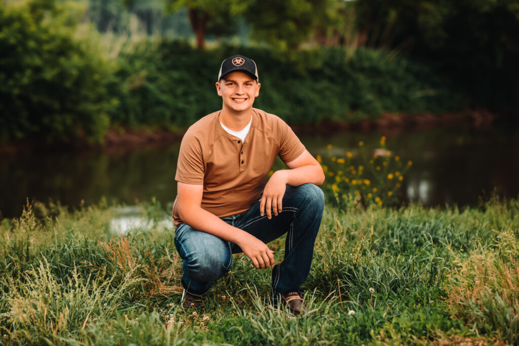 A high school senior squatting next to a creek during his senior photography experience.