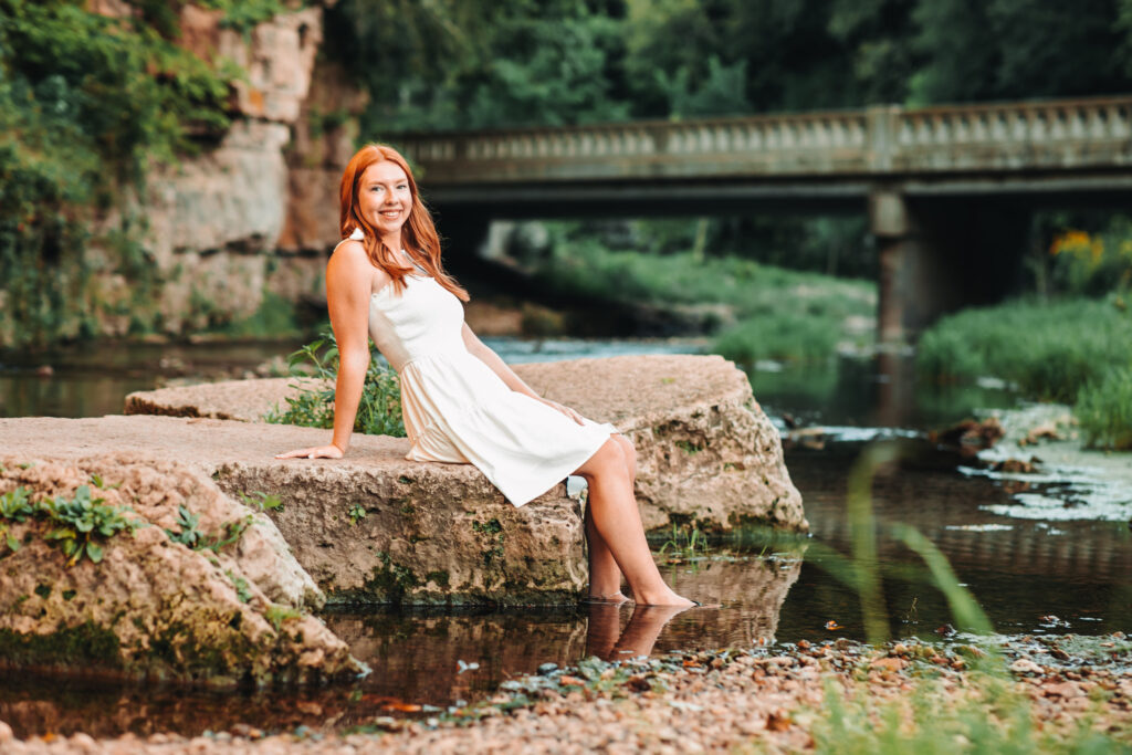 High school senior girl posing on a rock in a creek.
