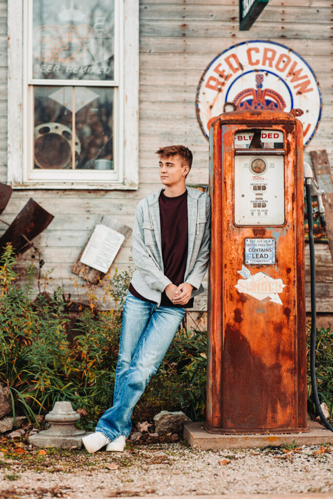 A high school senior standing next to a gas pump during his senior photography experience.