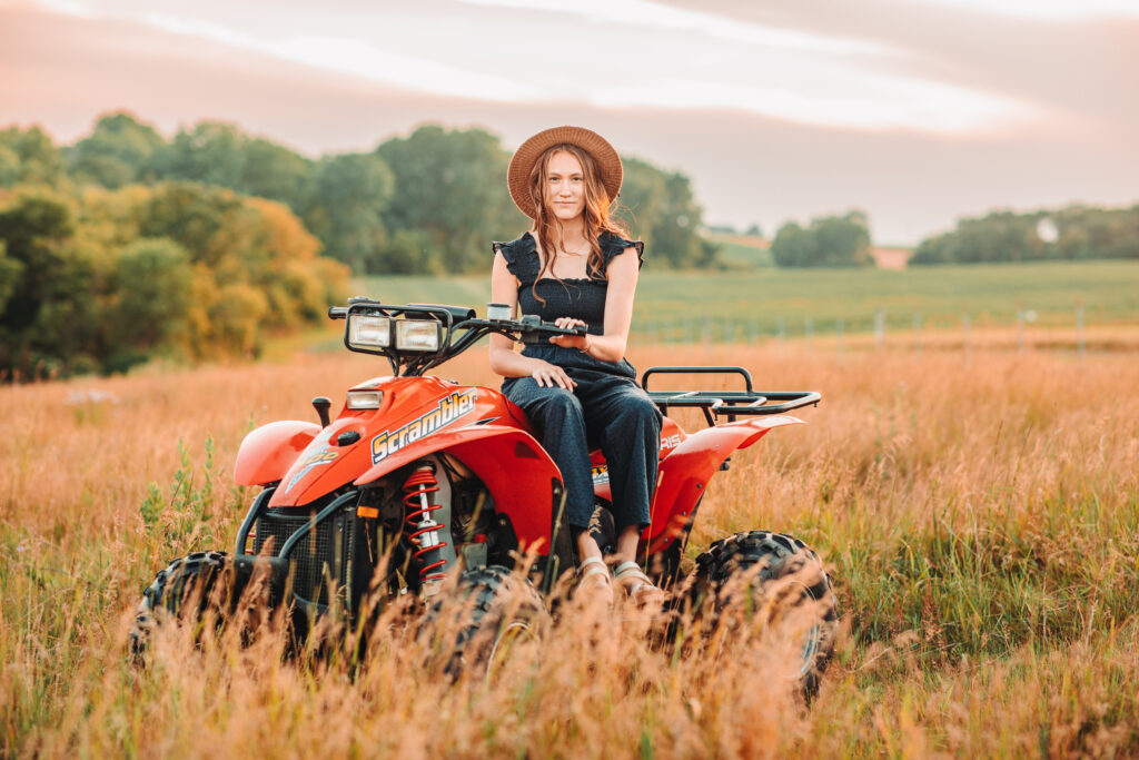 High school senior girl posing on her atv in the middle of a tall grassy field. 
