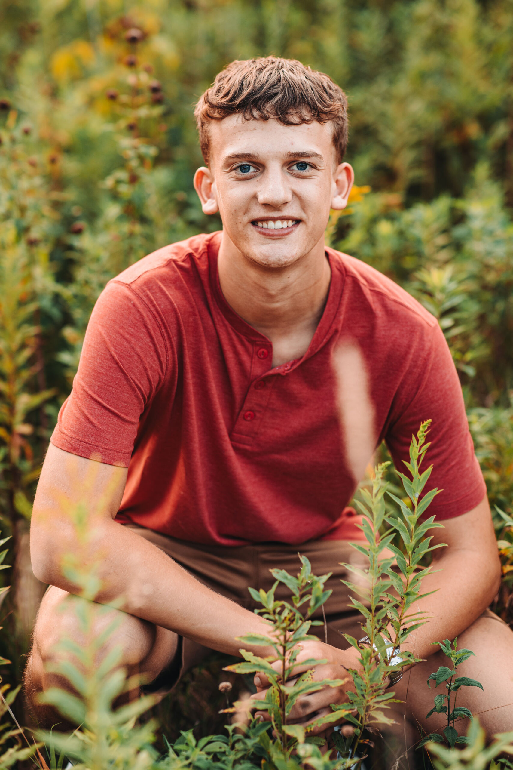 High school senior guy posing in a tall grassy field.