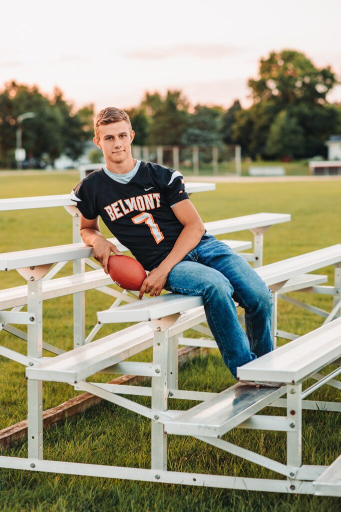 a high school senior guy sitting on the bleachers at his home football field