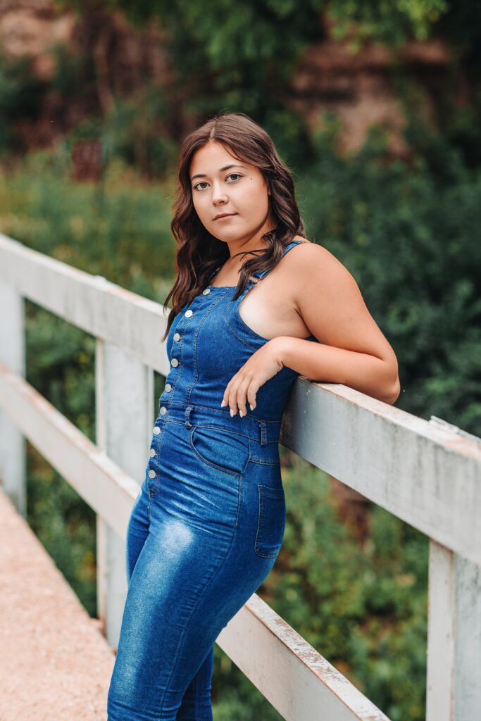 high school senior girl in blue jean jumper standing on a bridge