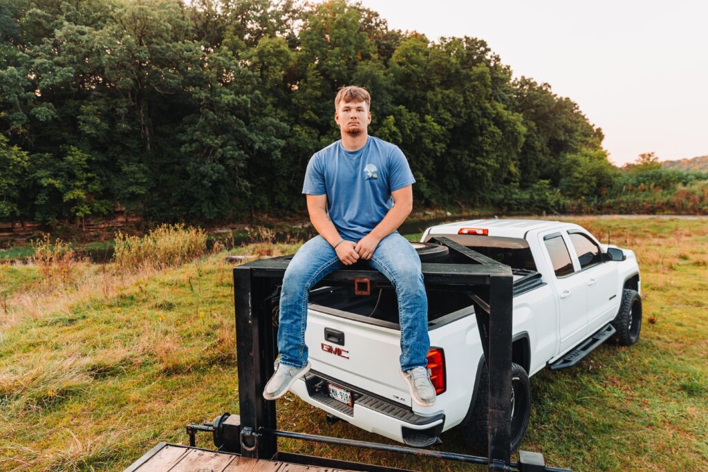 a high school senior guy sitting on his truck in a field