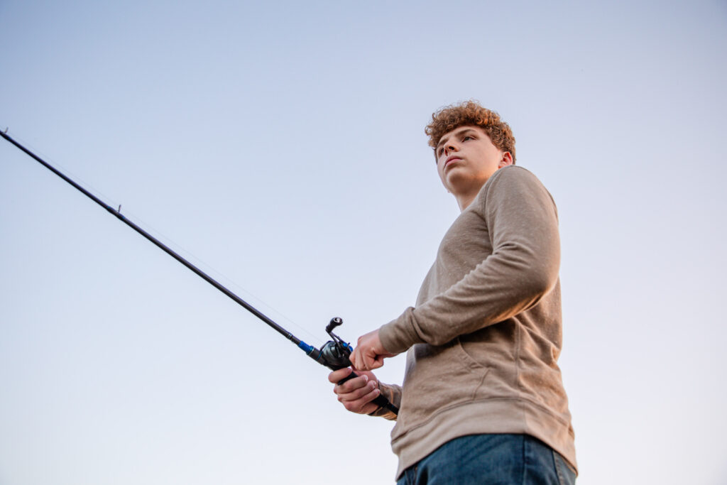Senior boy fishing during his personalized photo session on a riverbank had no idea what they wanted