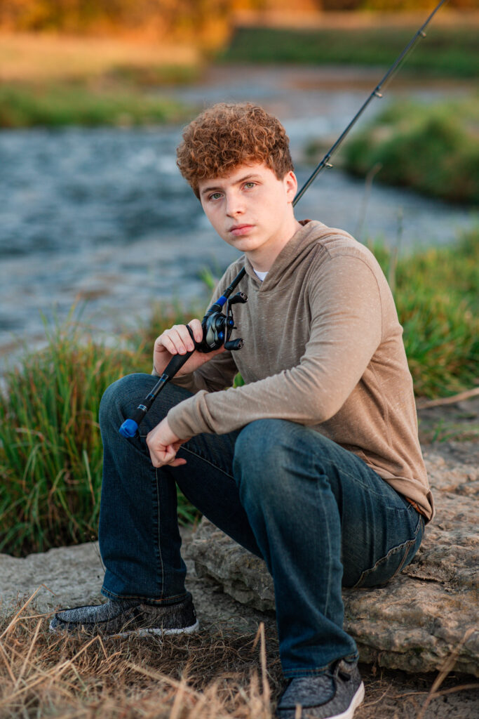 senior boy with is fishing pole on a river bank no idea what they want for senior session