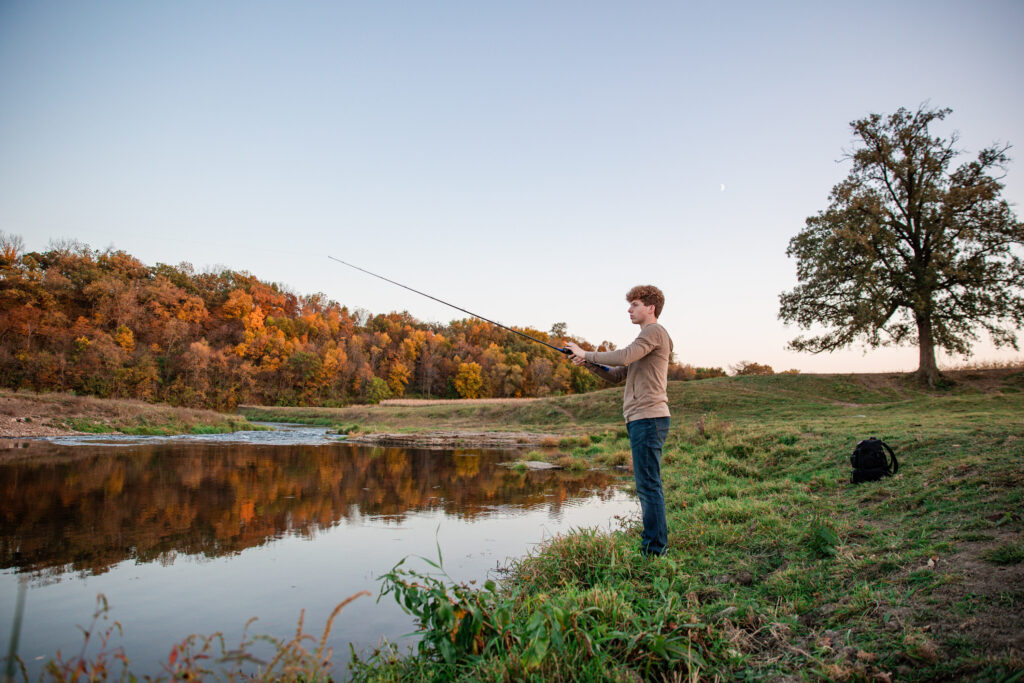 Senior boy fishing during his personalized photo session on a riverbank had no idea what they want